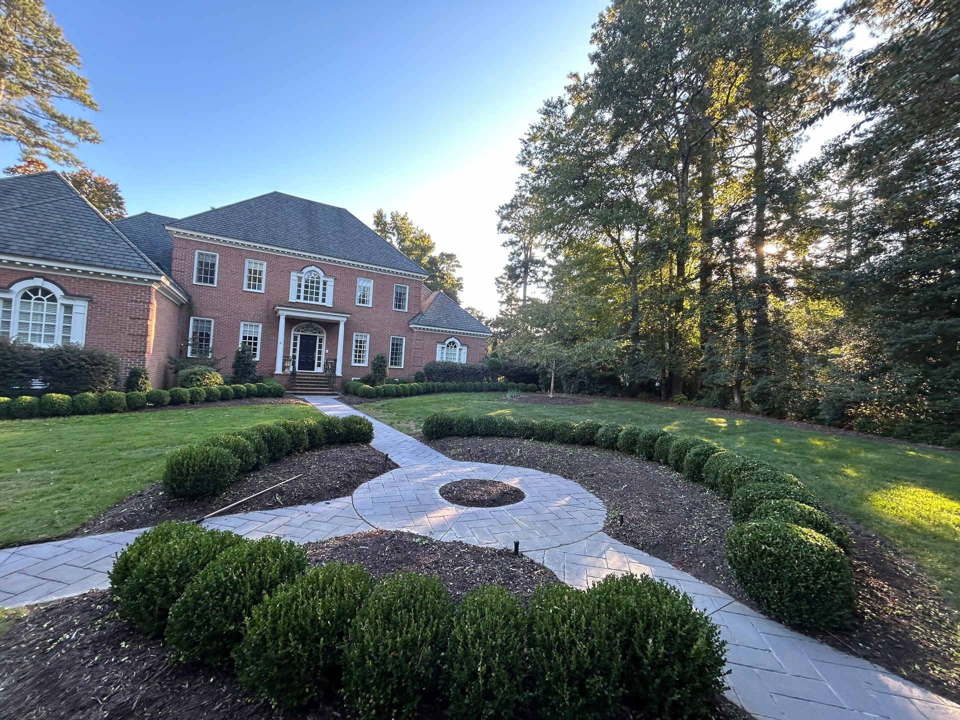 Brick house with manicured garden and winding gravel path at sunset