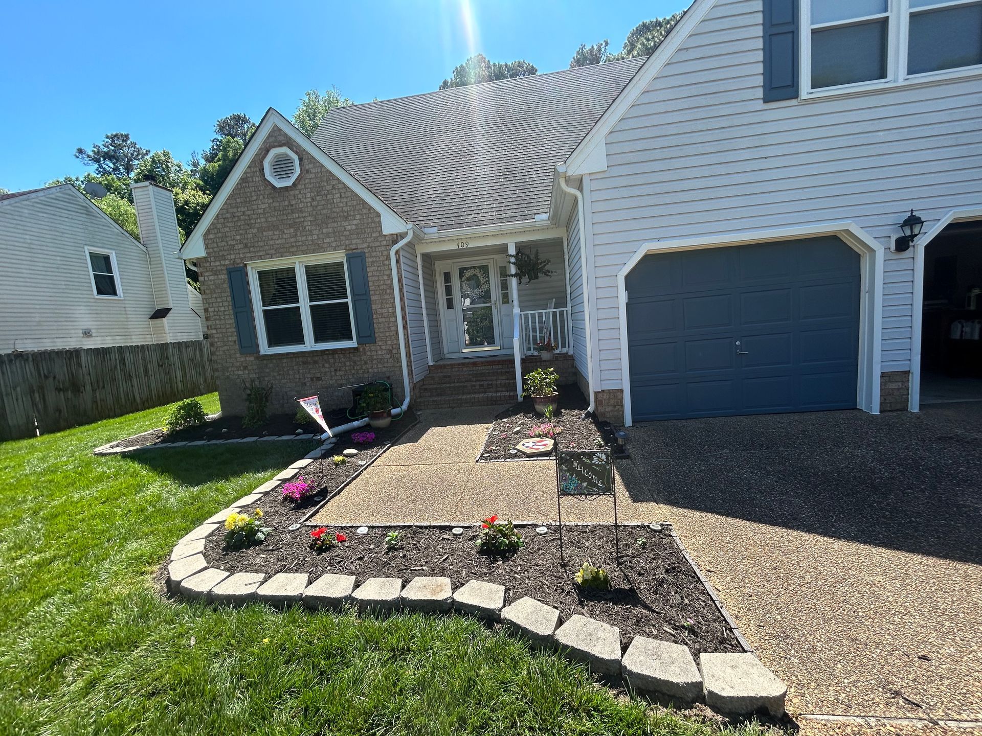 Suburban house with stone walkway, flower bed, and blue garage under bright sunlight