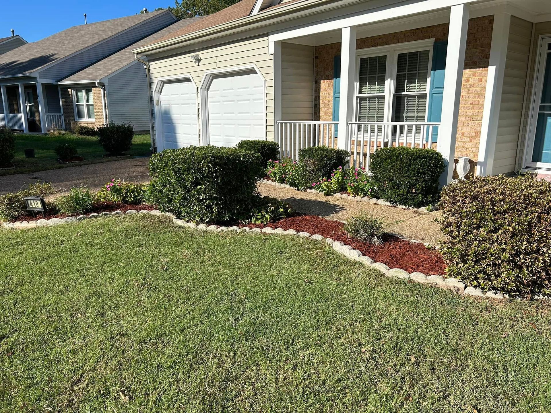 Suburban house with garage, front porch, and landscaped lawn under bright sunlight