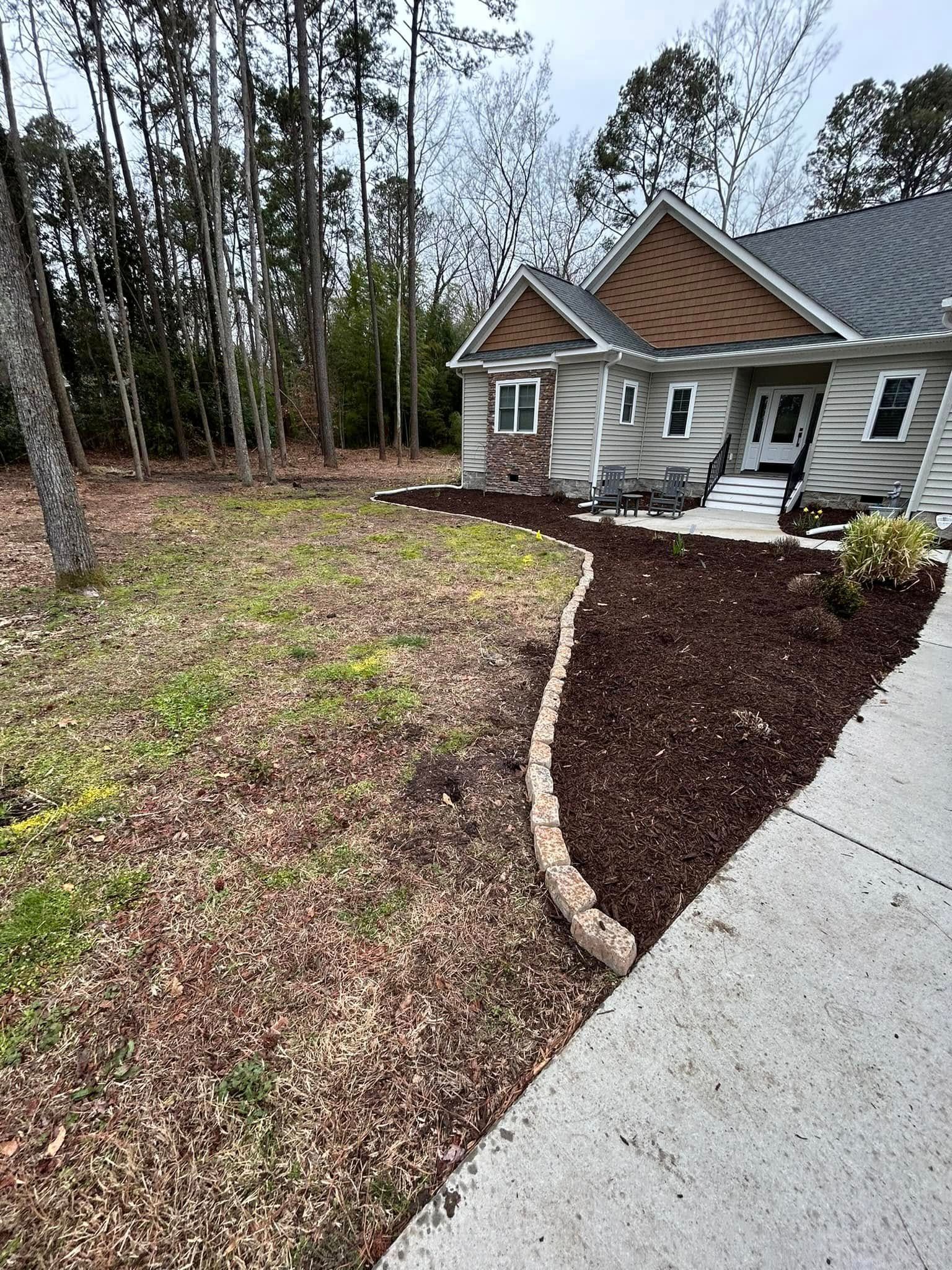 Front yard landscaping with fresh mulch beds, a curved stone border, and a concrete driveway beside a house.