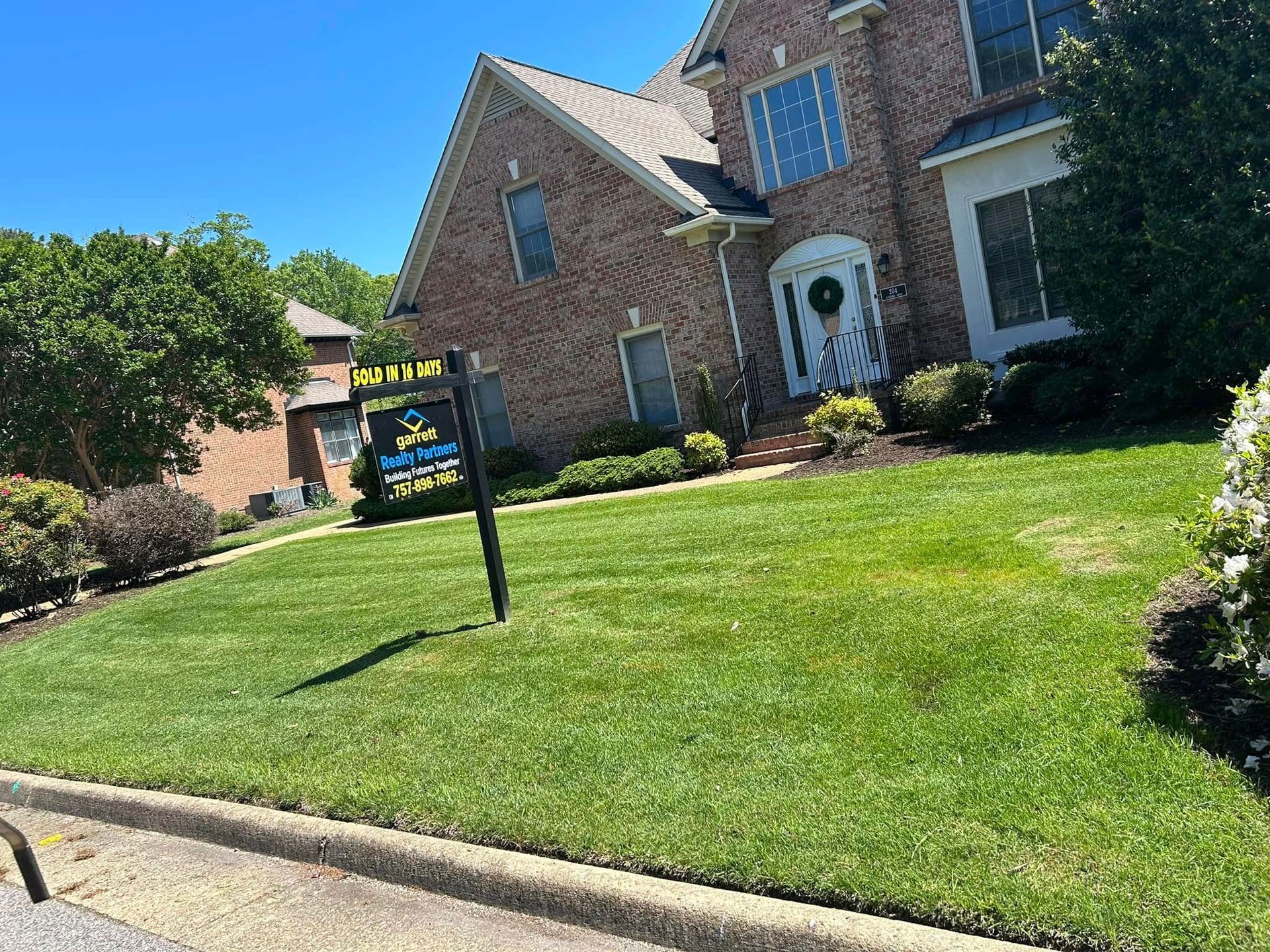 Suburban brick house with a manicured lawn and a real estate sign by the curb