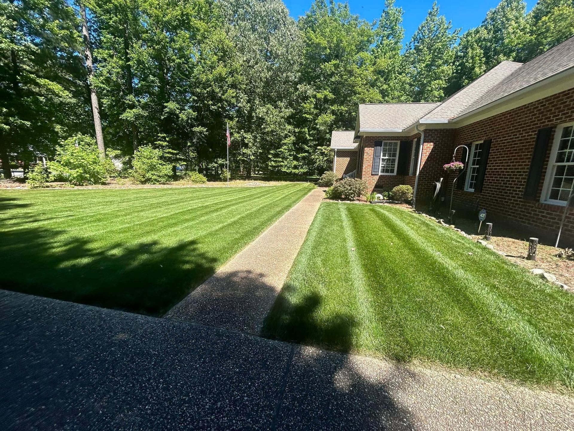 Brick house with a manicured lawn, gravel path, and trees in bright sunlight