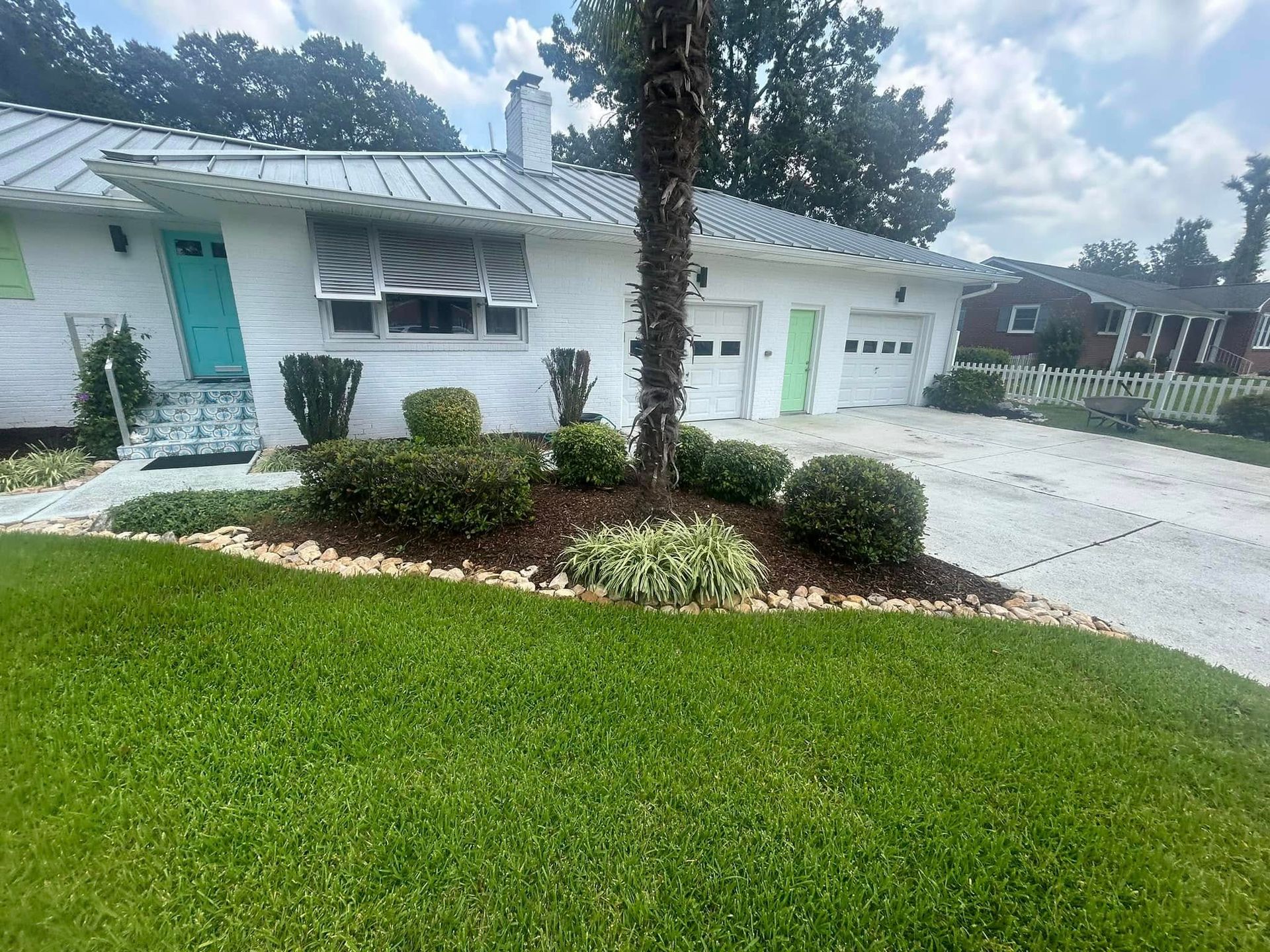 Single-story white house with green shutters, garage, palm tree, and landscaped lawn