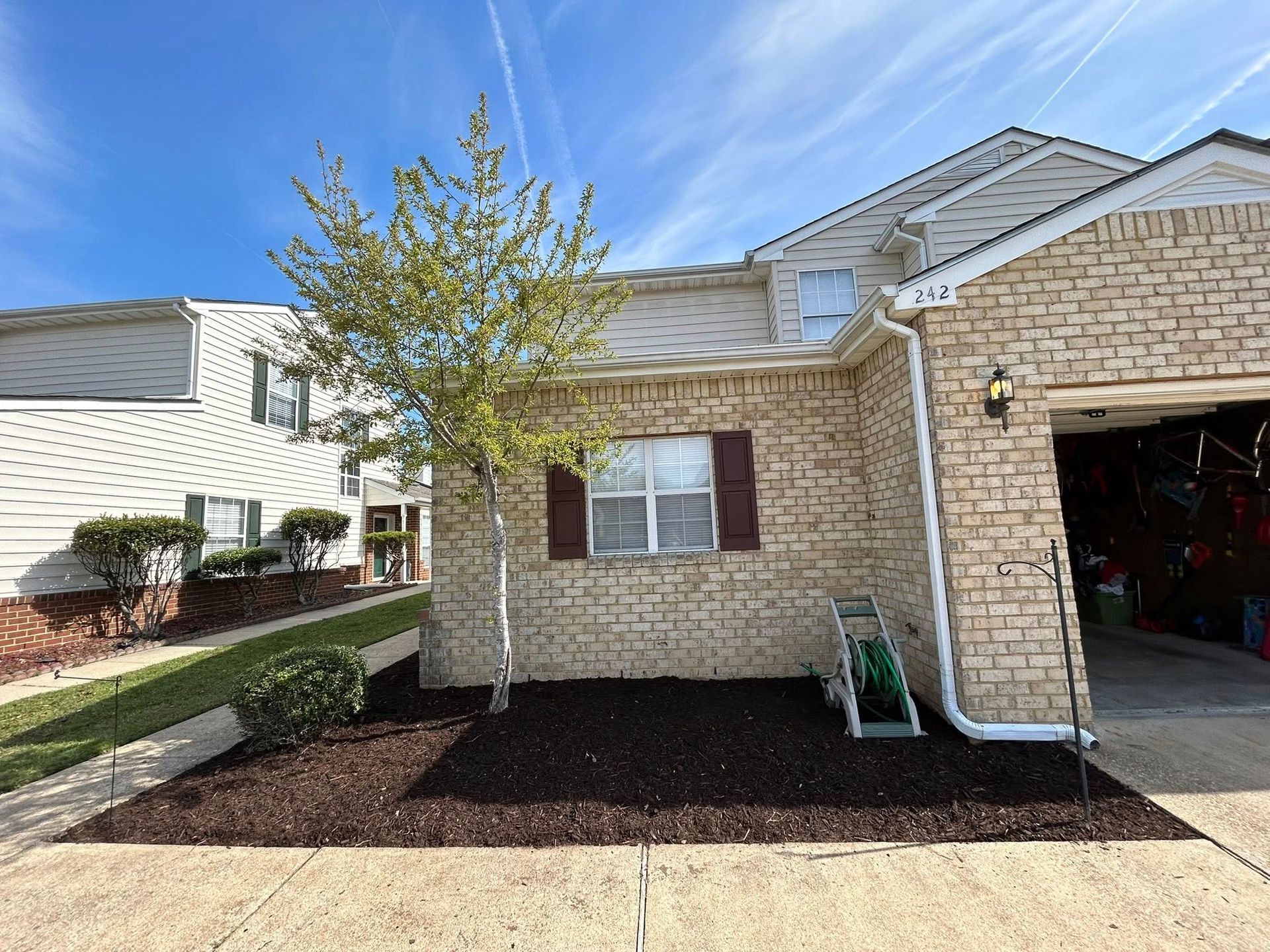 Brick townhouse exterior with small tree, front window, and open garage on a sunny day