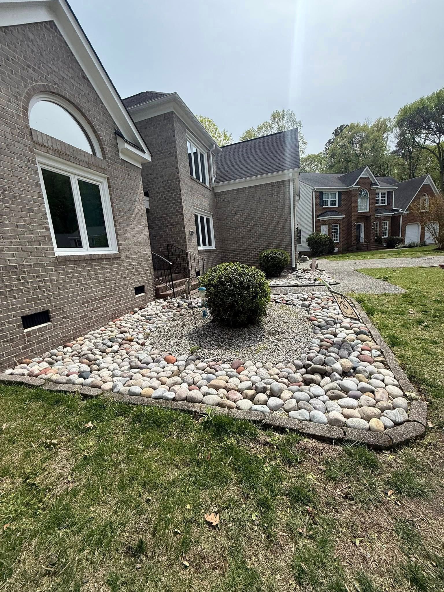 Landscaped stone bed with shrubs beside a brick house and grassy yard
