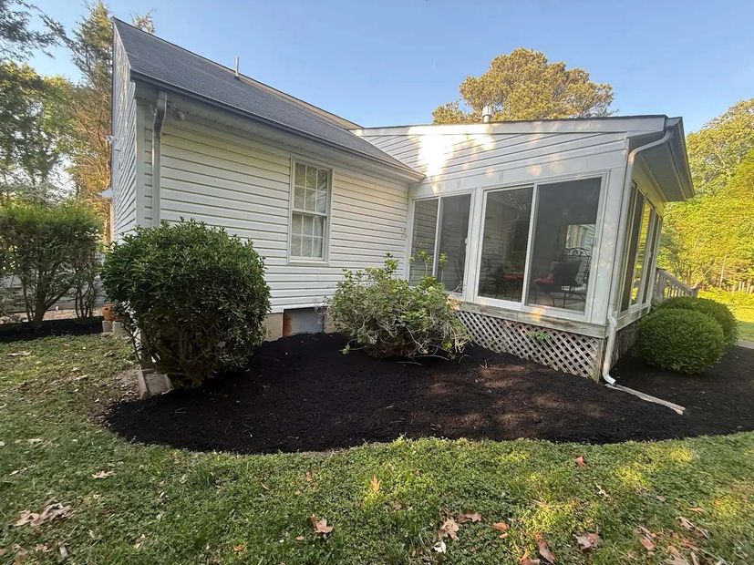 White house exterior with screened porch, bushes, and fresh black mulch in the front yard