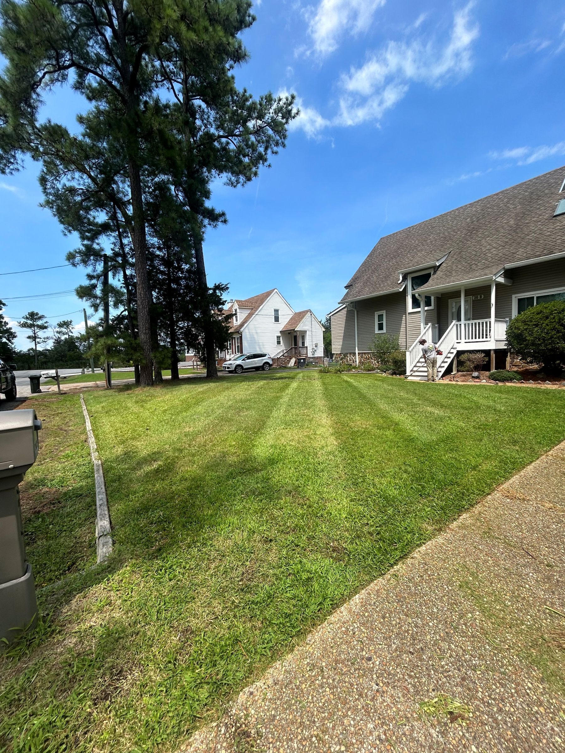 Grassy front yard beside a stone house and gravel driveway under a blue sky