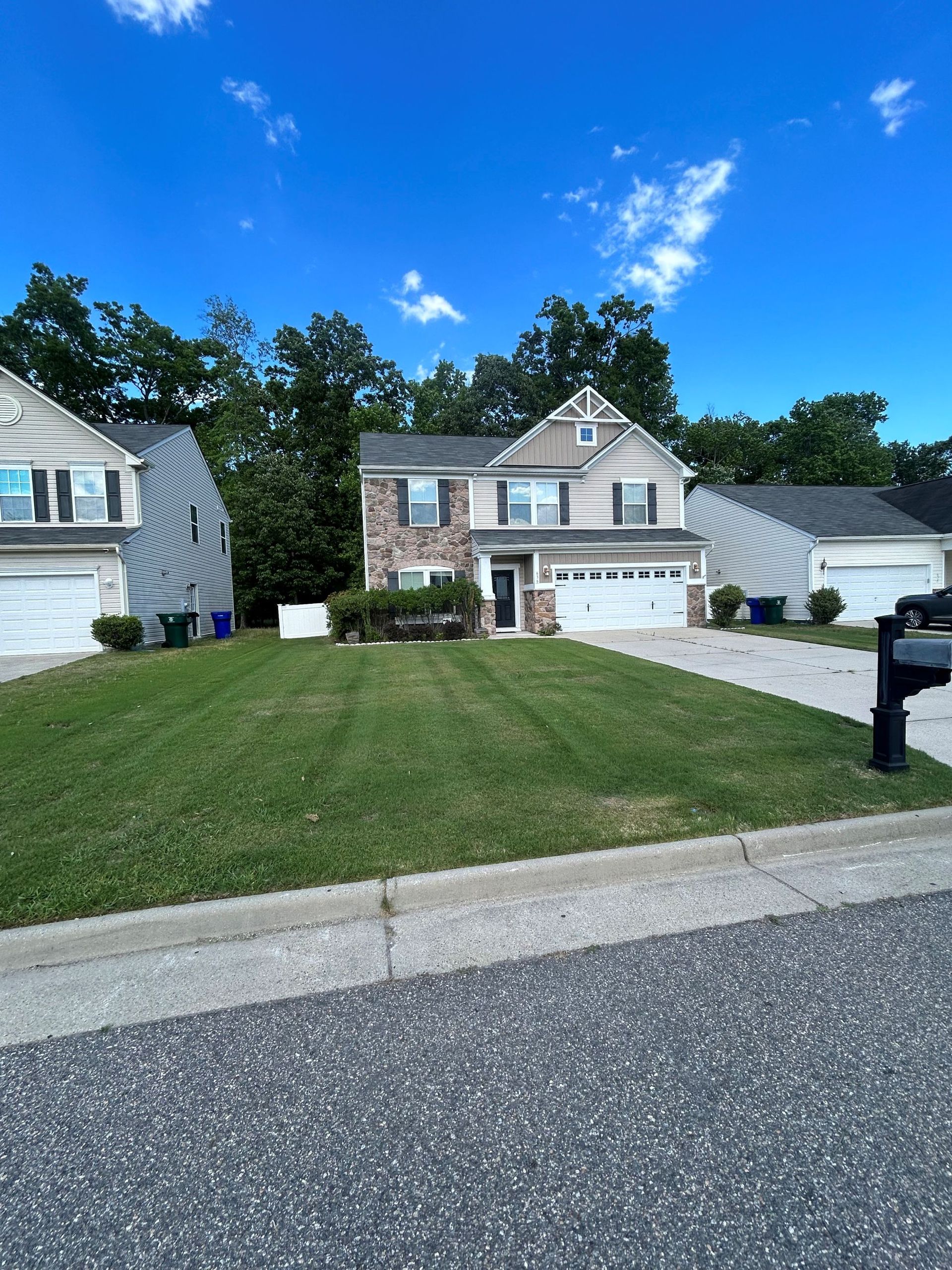 Suburban house with a brick facade, green lawn, driveway, and blue sky on a sunny day