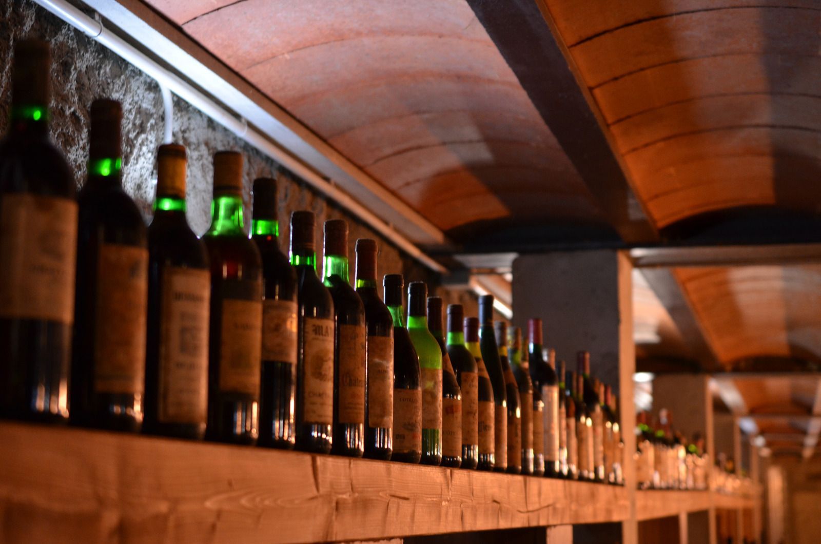 Many bottles of wine are lined up on a wooden shelf