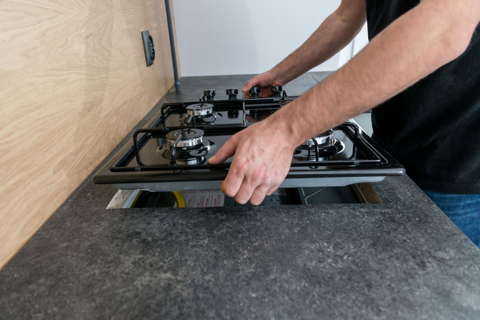 A person installing a black gas stovetop into a countertop with a cutout.
