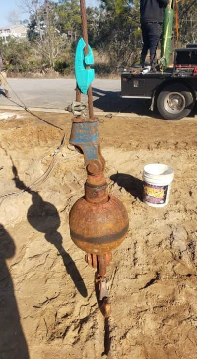 A rusty buoy is sitting in the dirt next to a truck with a Ropinator installed.
