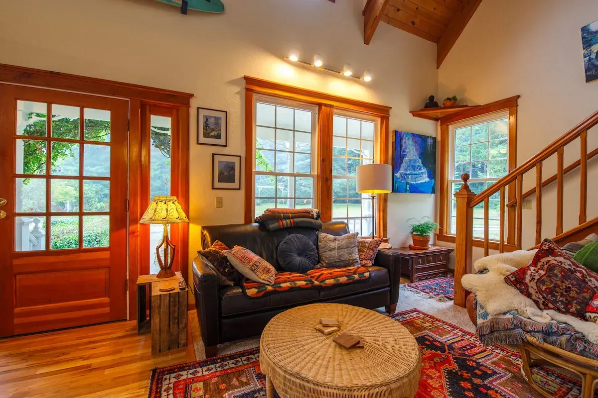 Cozy living room with dark leather sofa, colorful rugs, and wooden staircase.