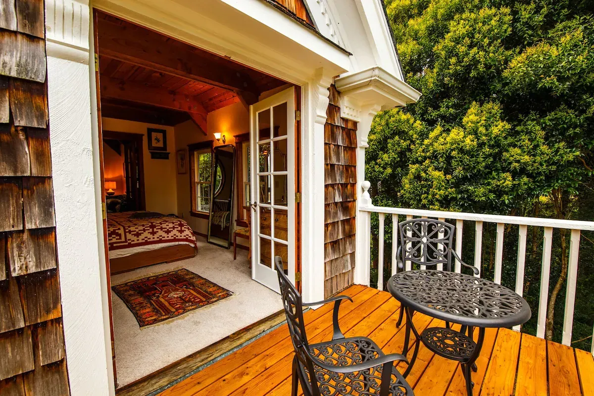 Balcony with iron table and chairs, leads to a bedroom. Brown wood shakes and decking.