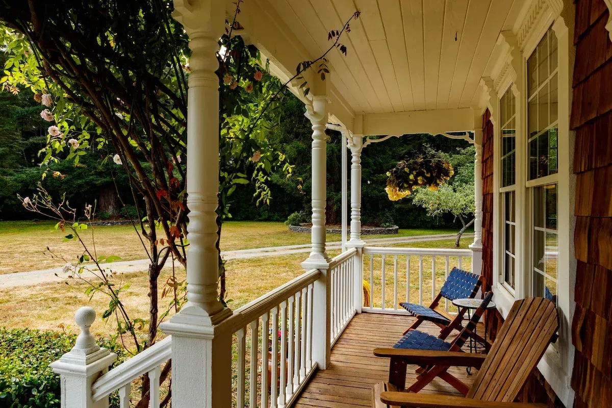 Porch of a house with white columns, brown chairs, and a garden view.
