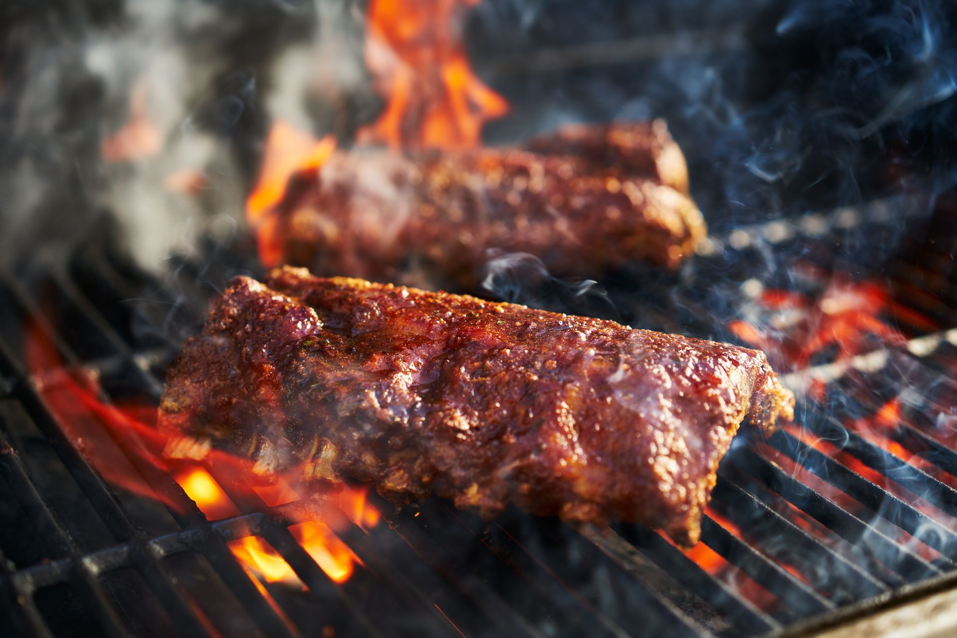 Ribs grilling on a hot barbecue with flames and smoke rising.
