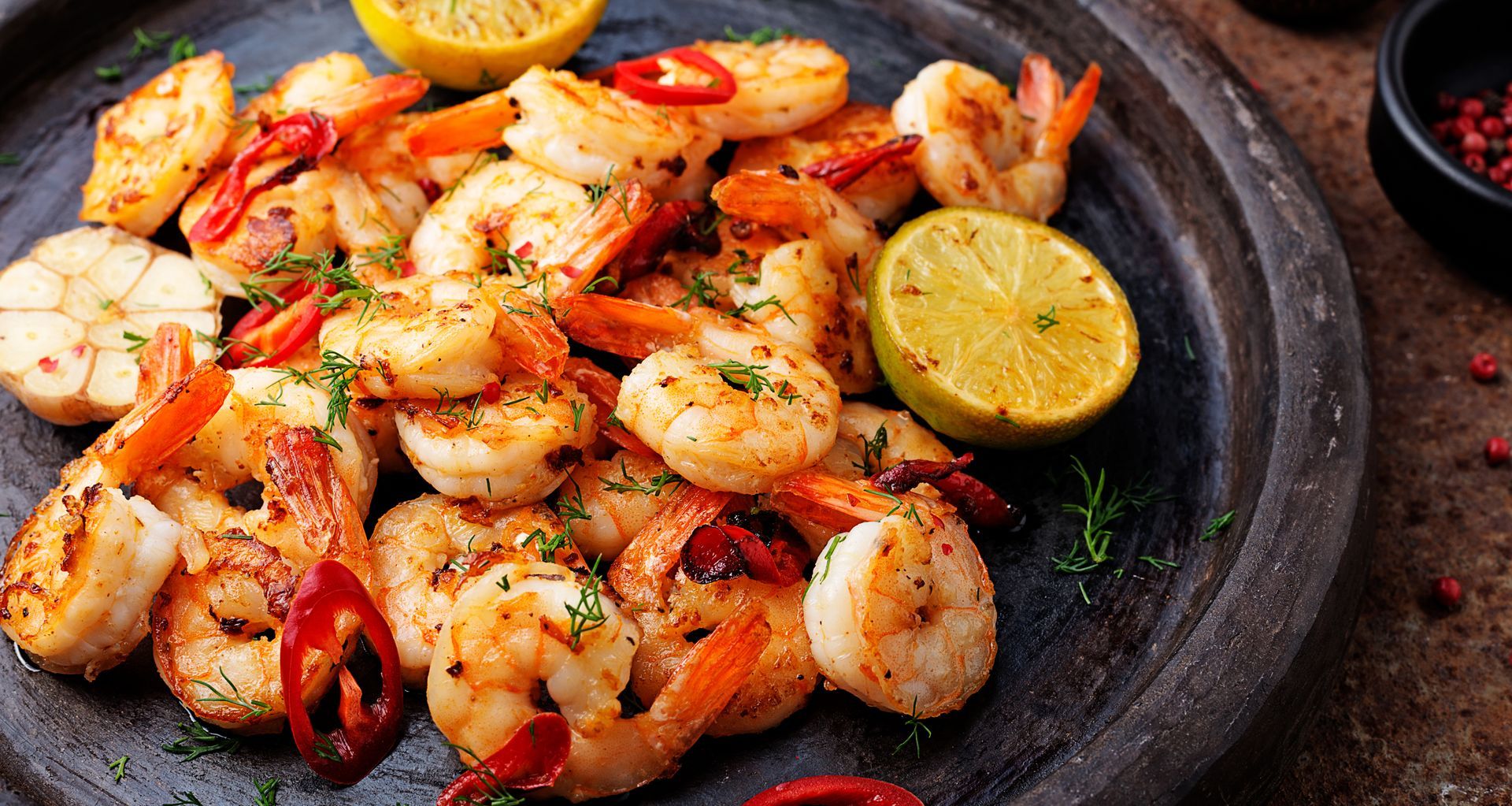 Sautéed shrimp with lemon wedges, red chili peppers, and herbs on a dark gray plate.