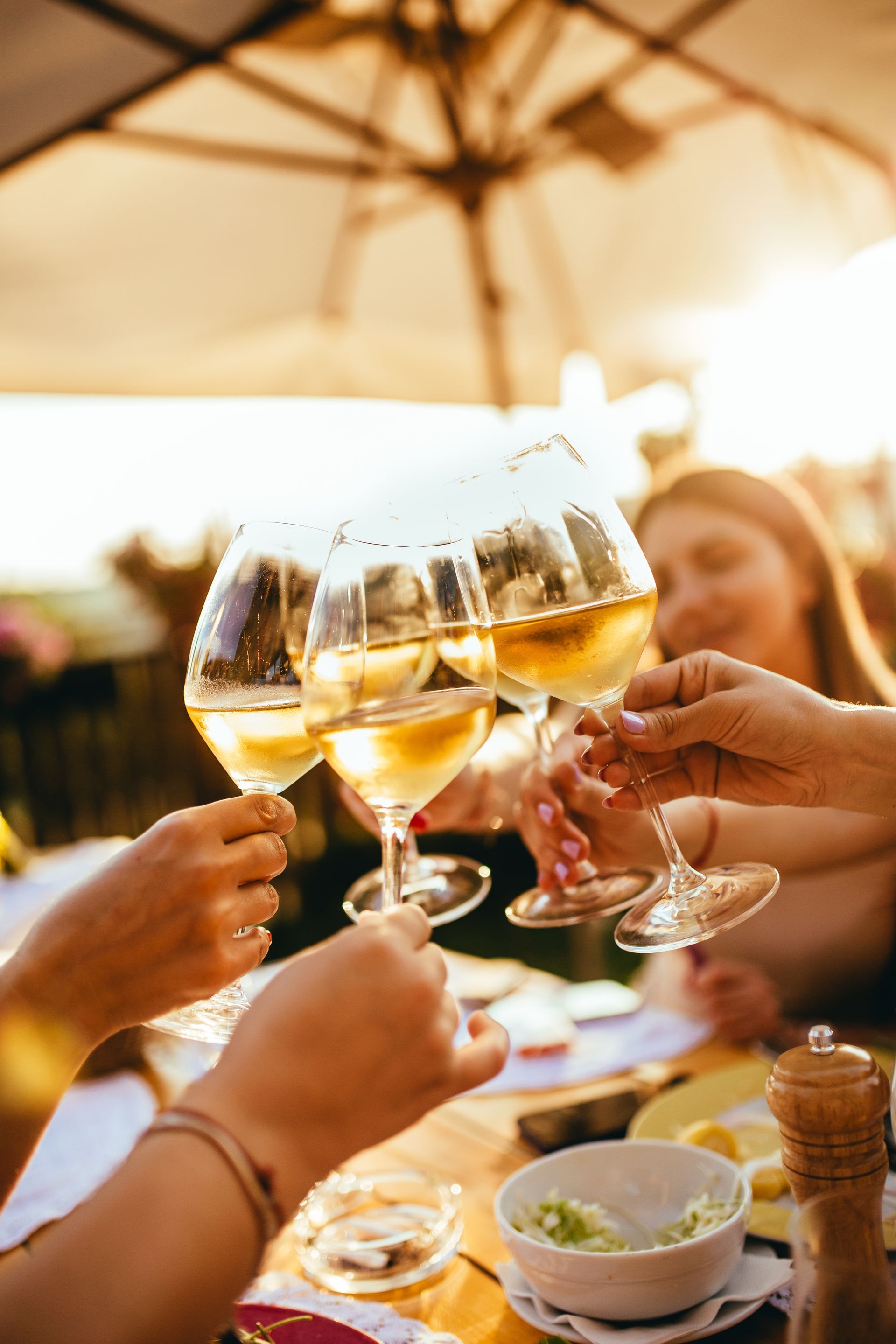 People toasting with white wine glasses at an outdoor table.