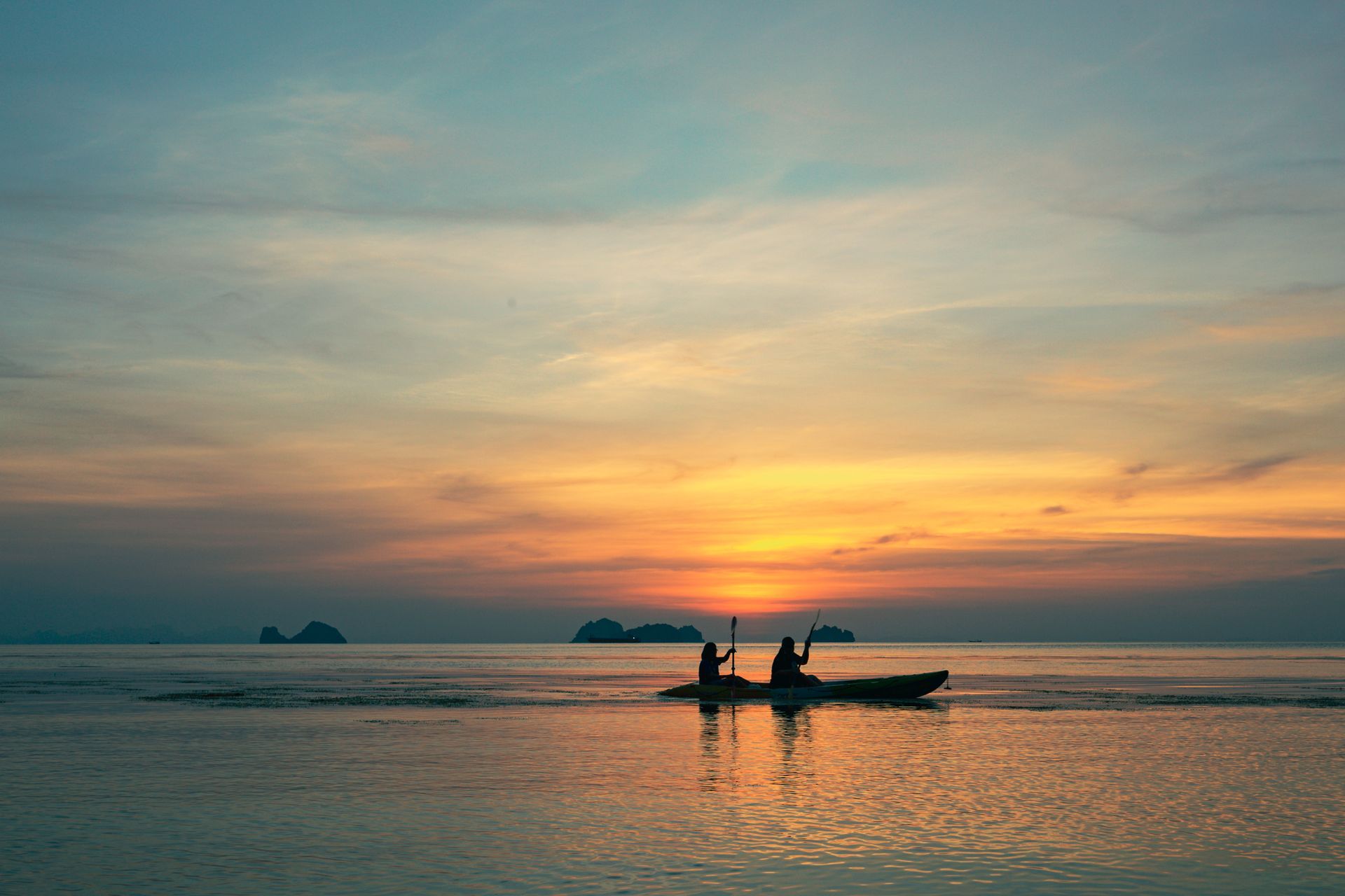 Silhouette of two people on a kayak, paddling into a sunset over the ocean.