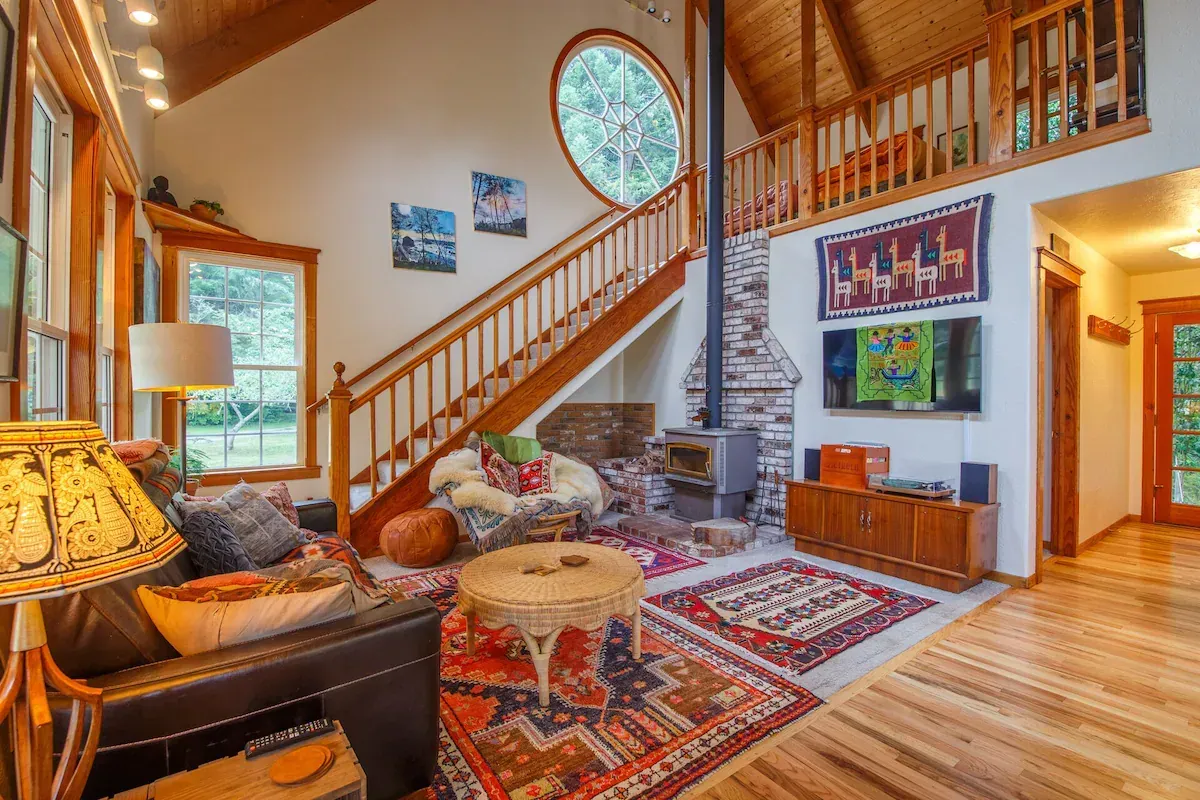 Cozy living room with a fireplace, stairs to a loft, and wood accents. Rugs, seating, and a TV.