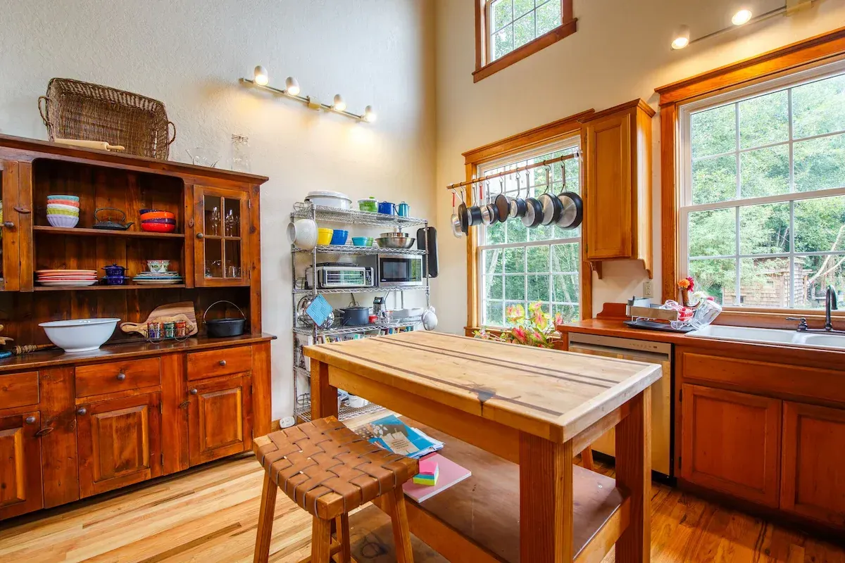 A cozy kitchen with wooden cabinets and island, windows, and a stainless steel rack.