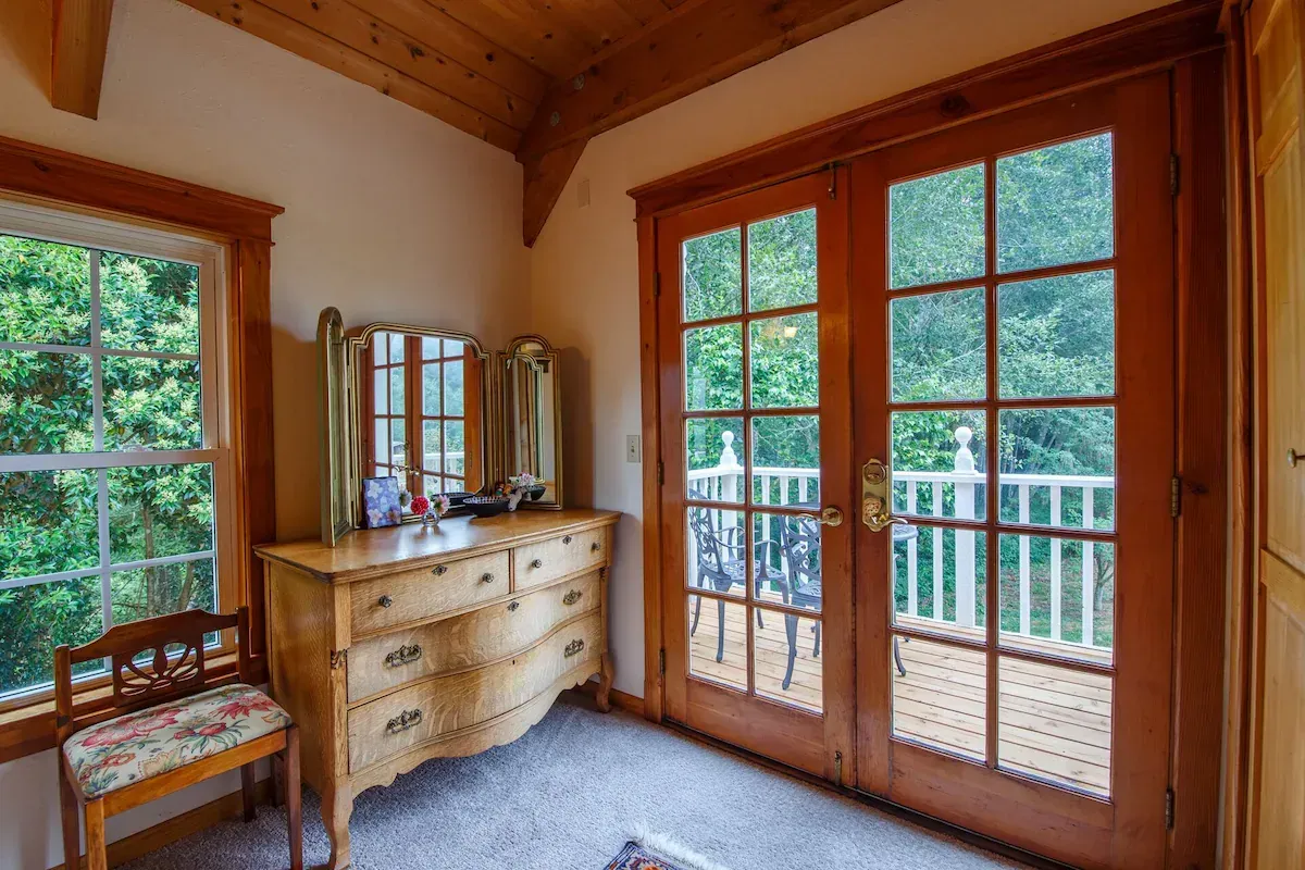 Bedroom with wooden trim, french doors to a balcony, a dresser, mirror, and chair. Bright and airy.