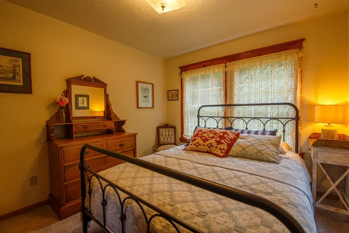Bedroom with antique furniture, iron bedframe, and lace curtains.