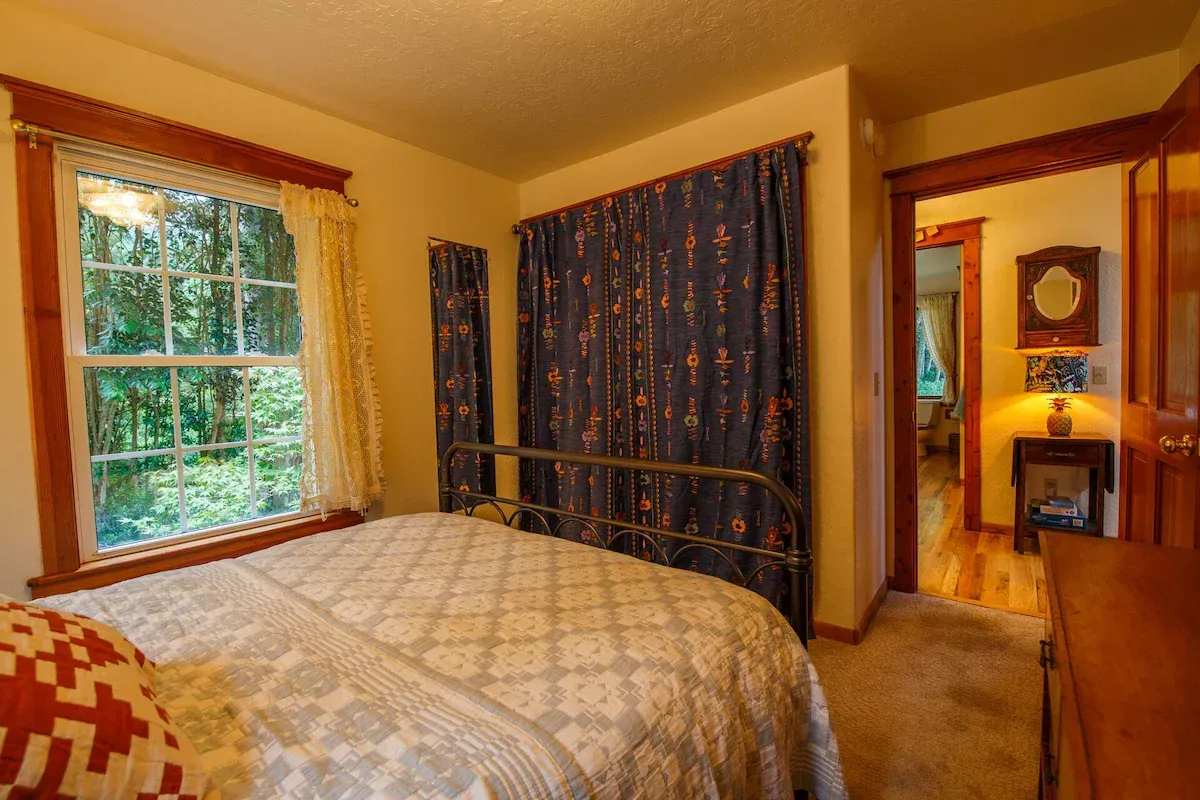 Bedroom with bed, window with view of trees, and doorway to another room.