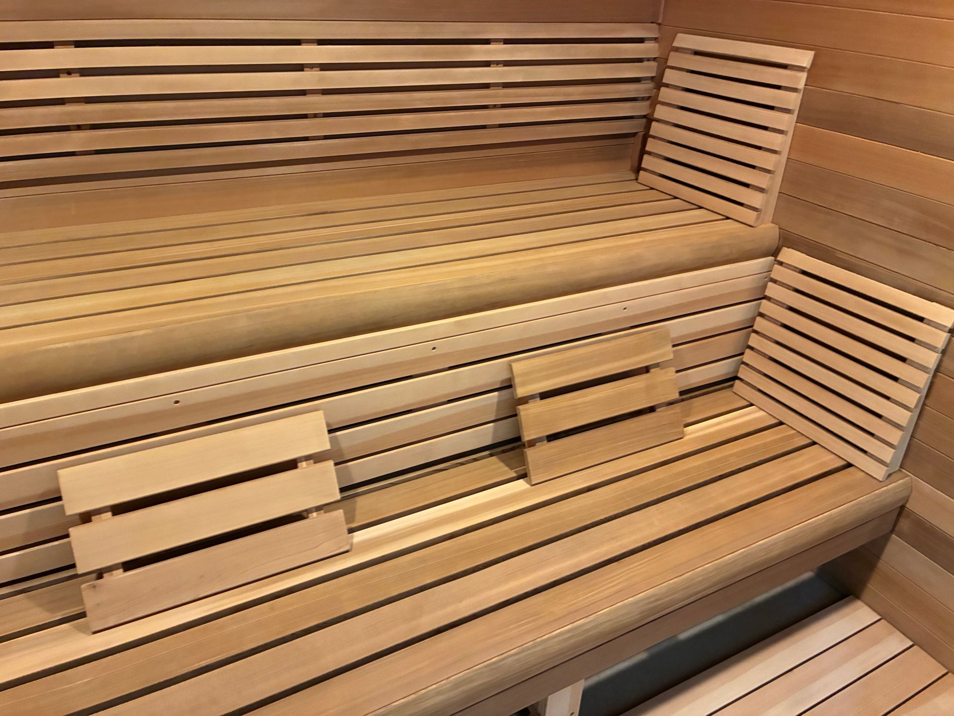 A wooden sauna with tiered bench seating and two small, slatted wooden backrests resting on the lower bench.