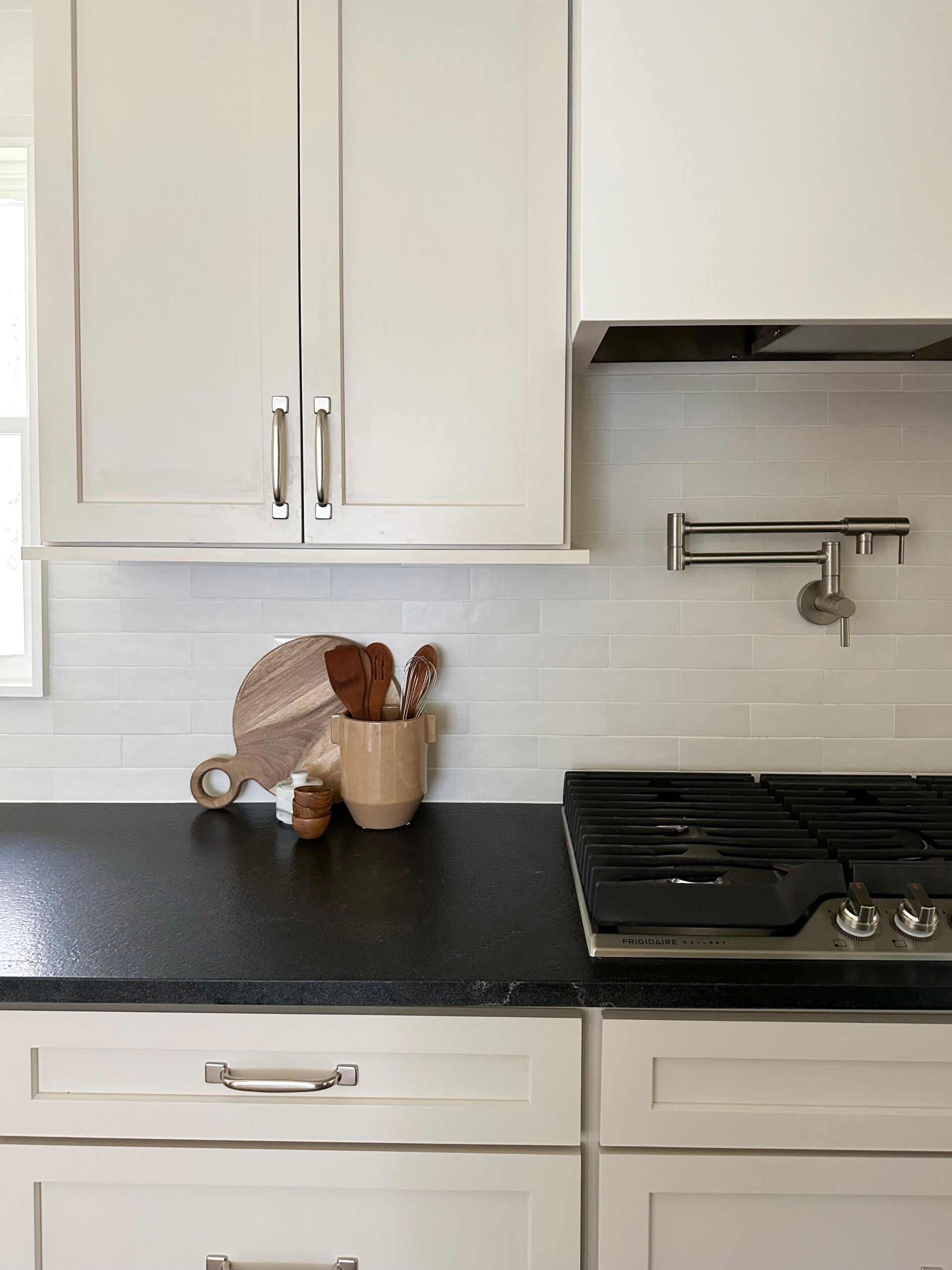 A kitchen with white cabinets, black countertops, a stove, a pot filler faucet, and a ceramic utensil holder on the counter.