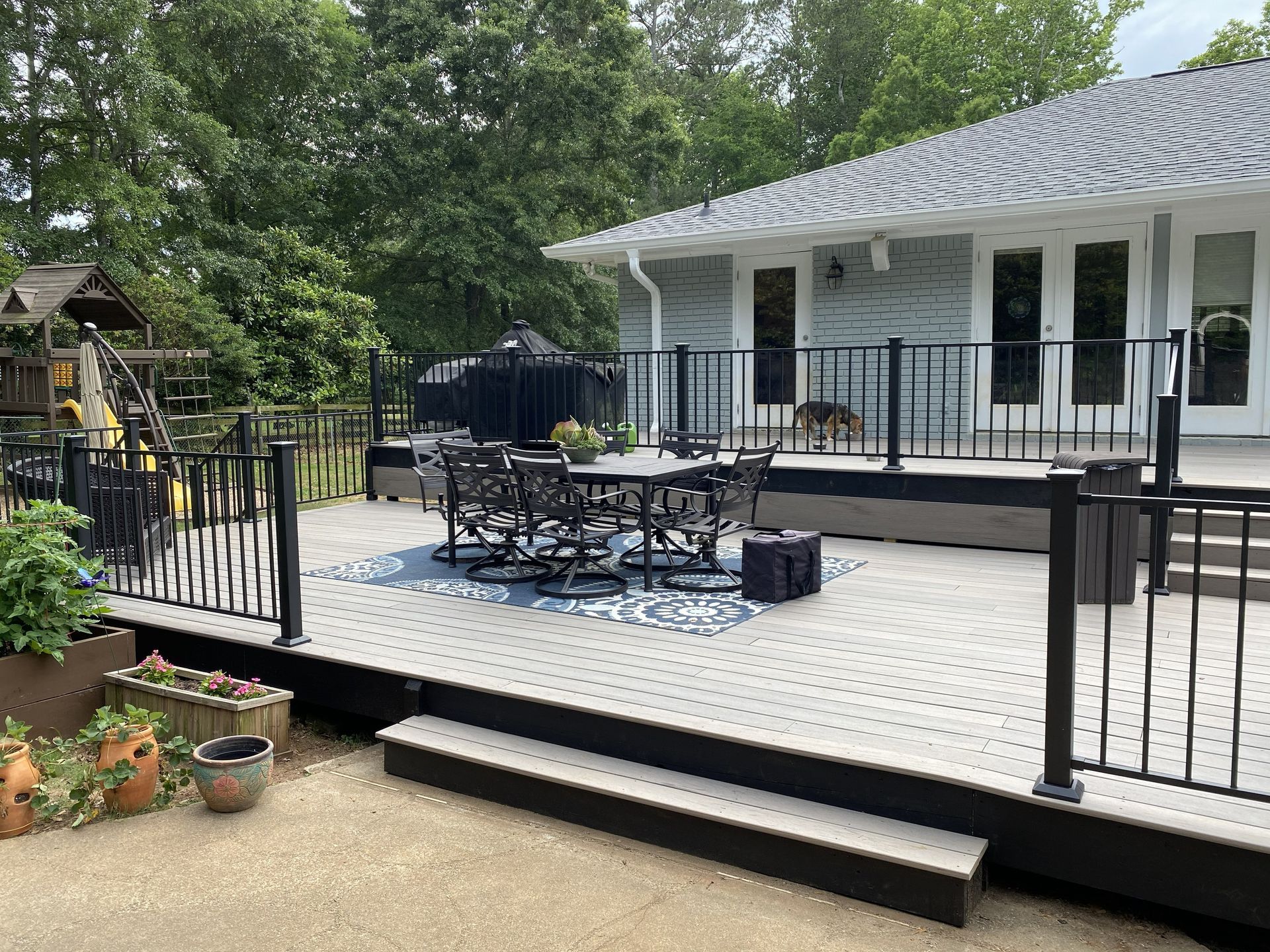 A large gray composite deck with black railings, a patio dining set, and stairs leading down to a concrete patio.