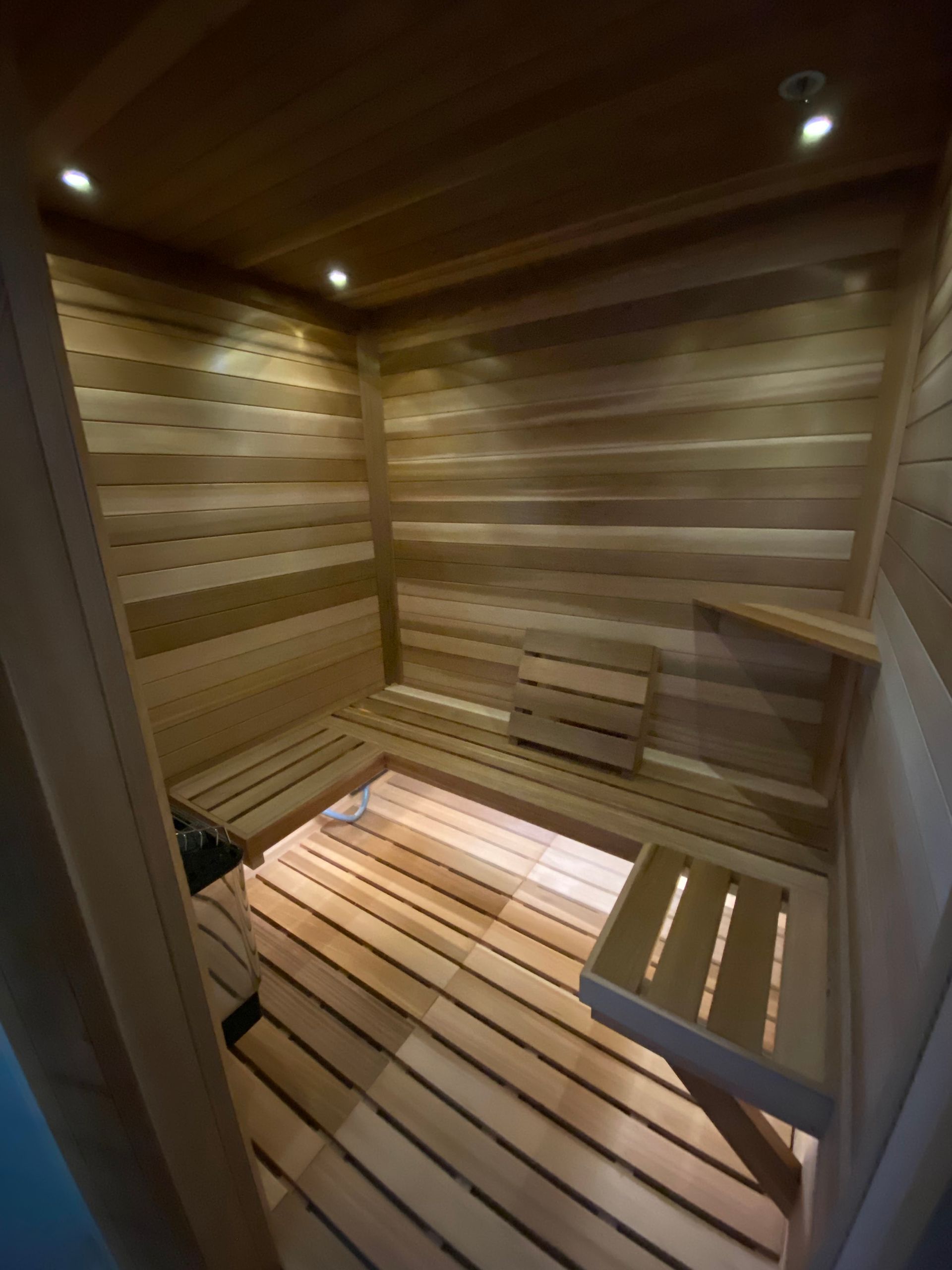 Interior of a small, wooden-walled home sauna featuring tiered benches and recessed ceiling lighting.