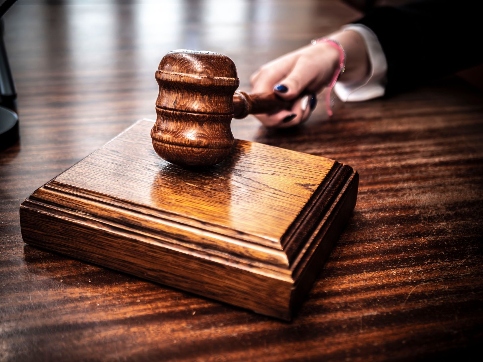 Judge’s gavel on a wooden block in a courtroom, with a hand holding the handle