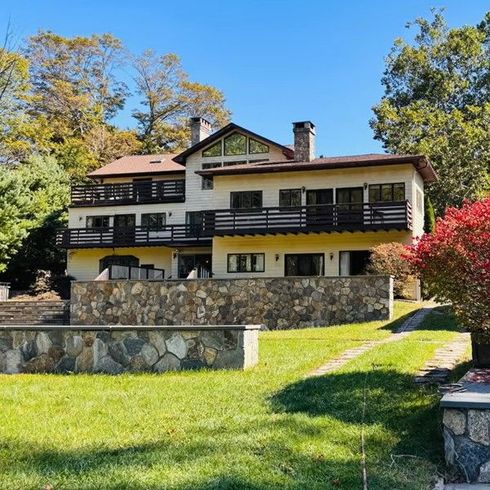 Large multi-level estate home with wraparound decks, stone retaining walls, and manicured lawn, surrounded by trees and a vintage lamppost, ready for estate cleanouts