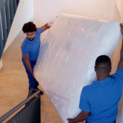 Two workers carrying a wrapped mattress down a staircase for mattress removal service