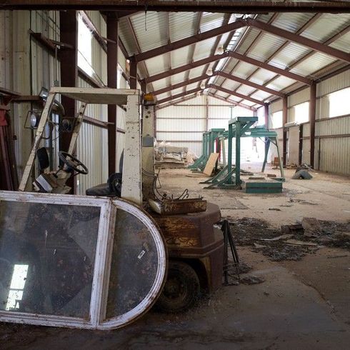 Old forklift and discarded window frame inside a cluttered warehouse ready for junk removal