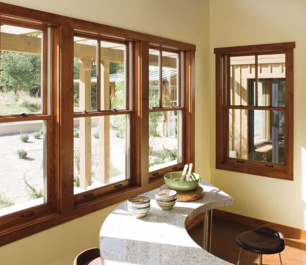 Bright dining nook with wooden windows, round table, and stools overlooking a garden patio