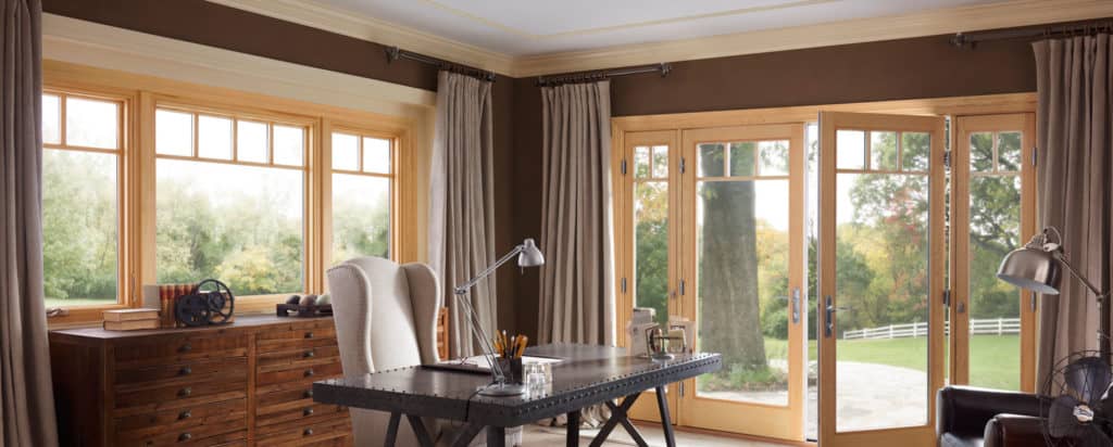 Sunlit living room with desk, chairs, wood dresser, and large windows opening to a garden