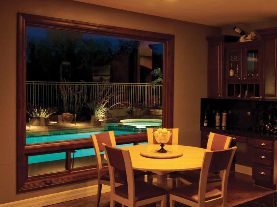 Dining area with round table overlooking a lit backyard pool at dusk