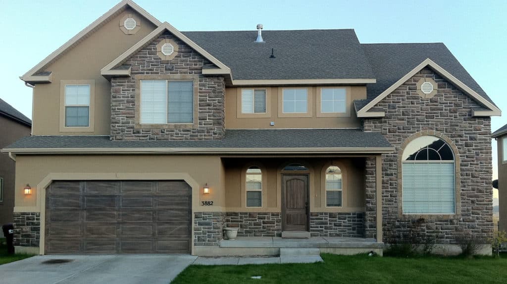 Two-story suburban house with stone accents, a garage, and a front porch at dusk