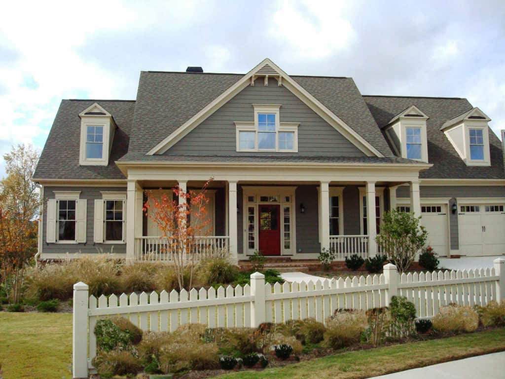 Large gray house with white trim, front porch, and picket fence in autumn