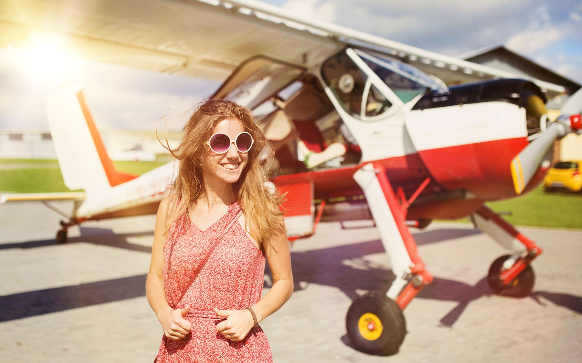 A woman in a red dress is standing in front of a small airplane.