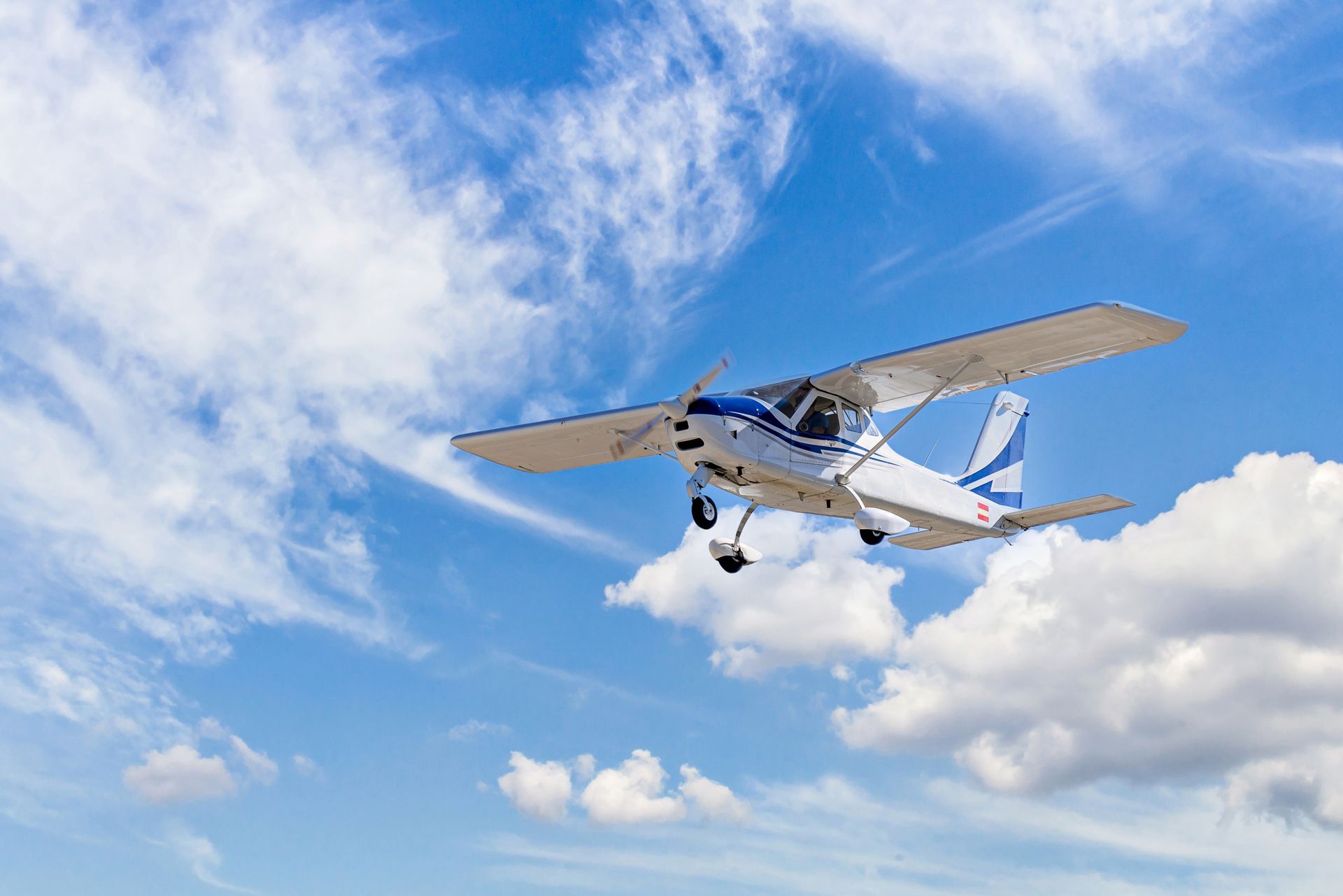 A small plane is flying through a cloudy blue sky.