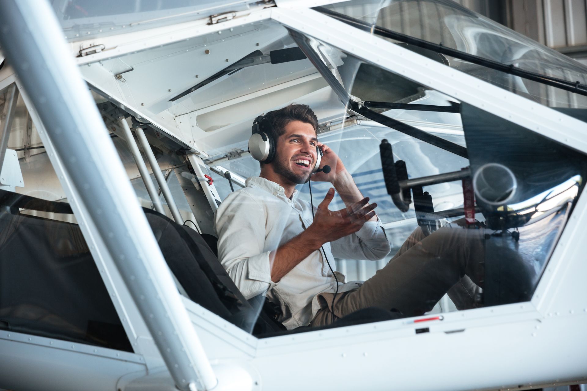 A man is sitting in the cockpit of an airplane talking on a cell phone.