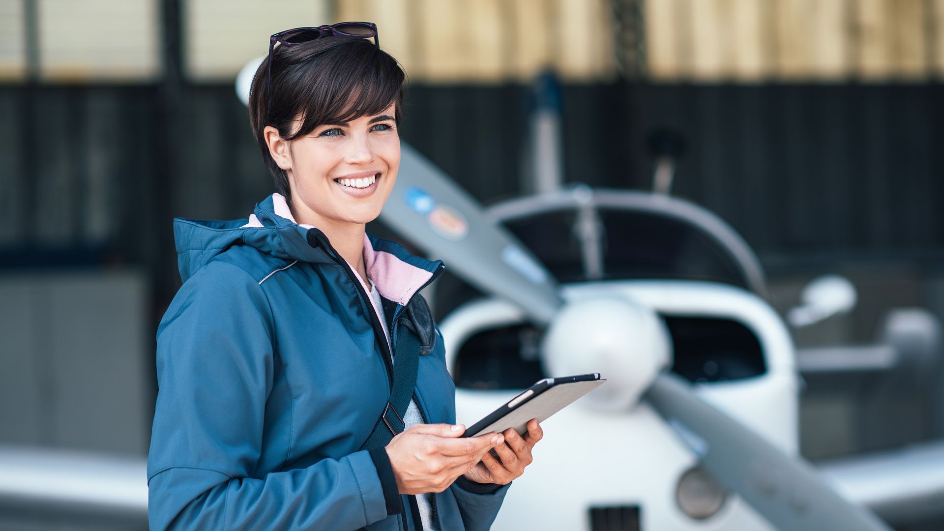 A woman is standing in front of a small plane holding a tablet.