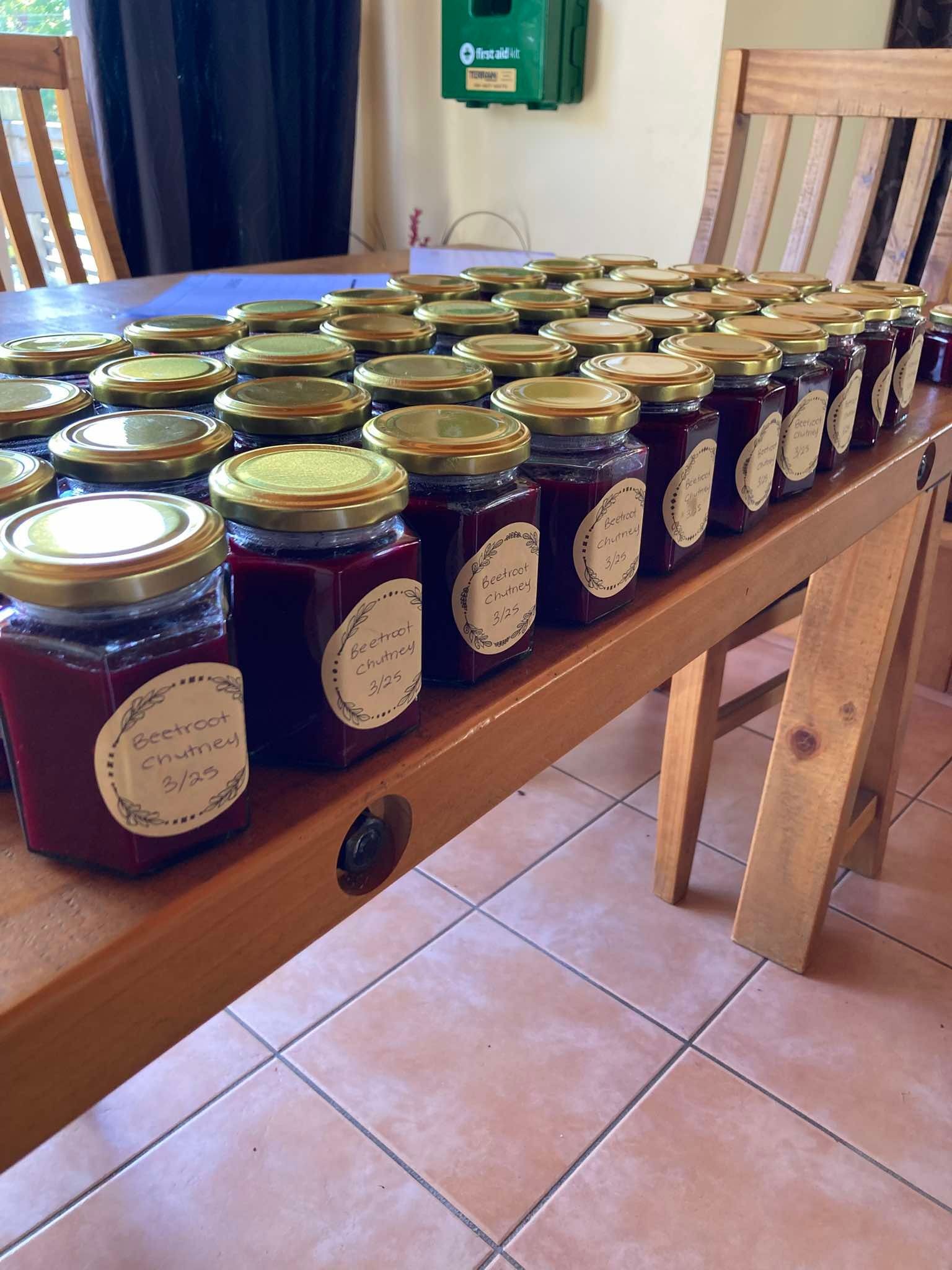 Rows of glass jars filled with red jam, each with a gold lid and label, lined up on a wooden table.
