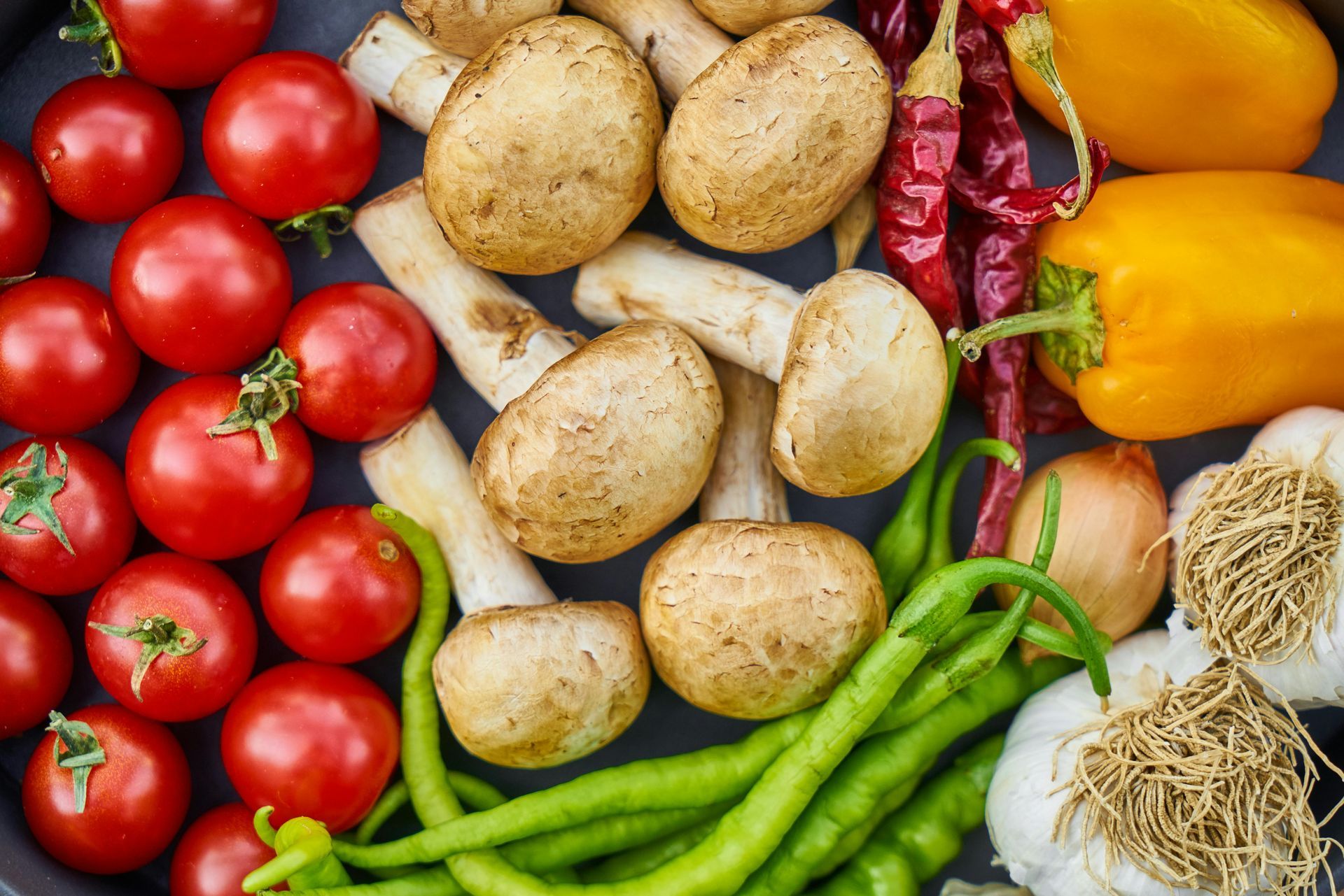 Fresh vegetables: tomatoes, mushrooms, bell peppers, chilies, garlic, and green peppers, in vibrant colors.