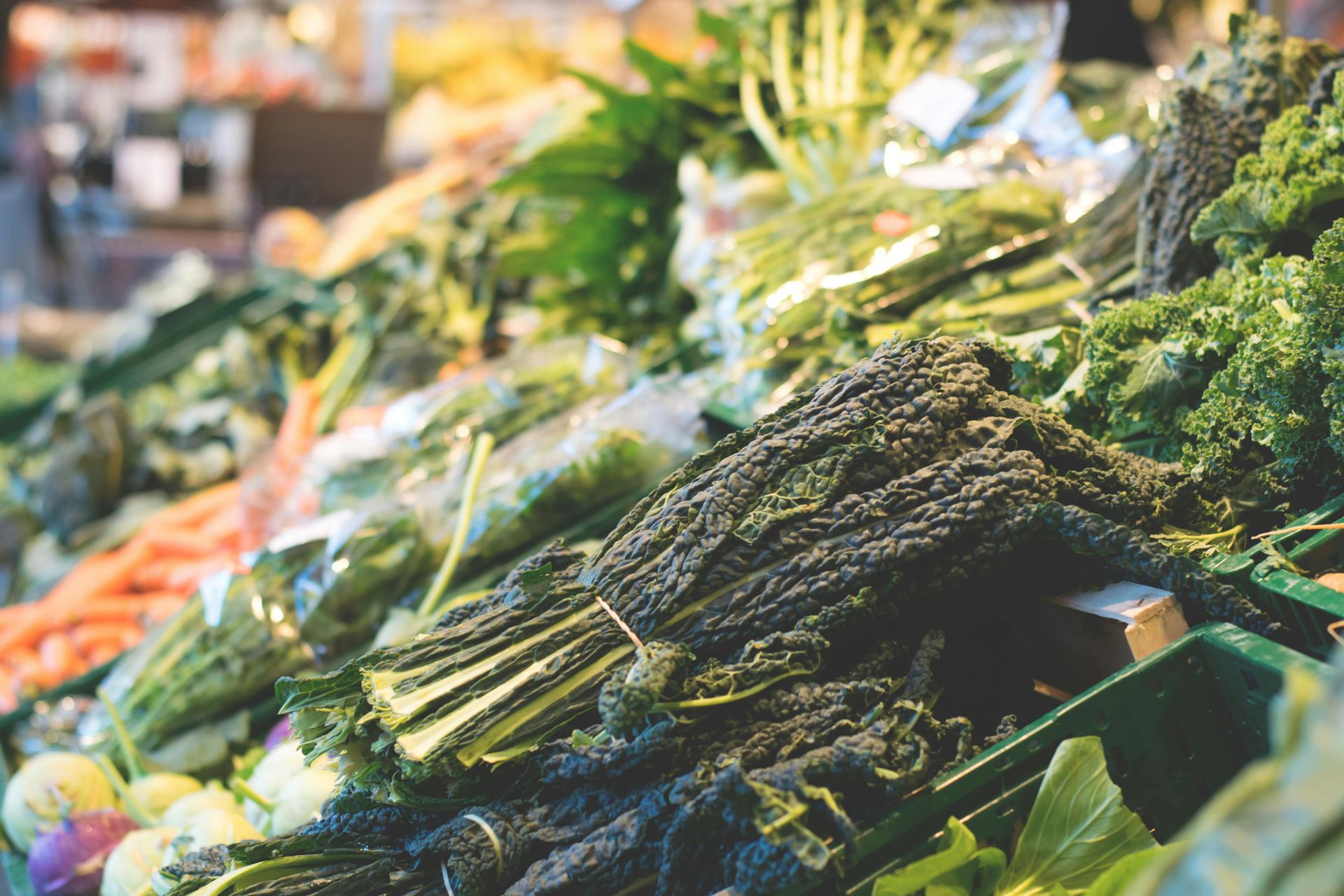 Produce stand displaying various fresh, green vegetables and some orange carrots.