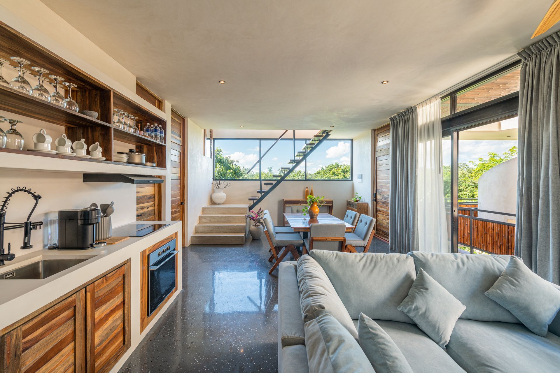 Modern living room with gray sofa, kitchen bar, stairs, and ocean view through large windows