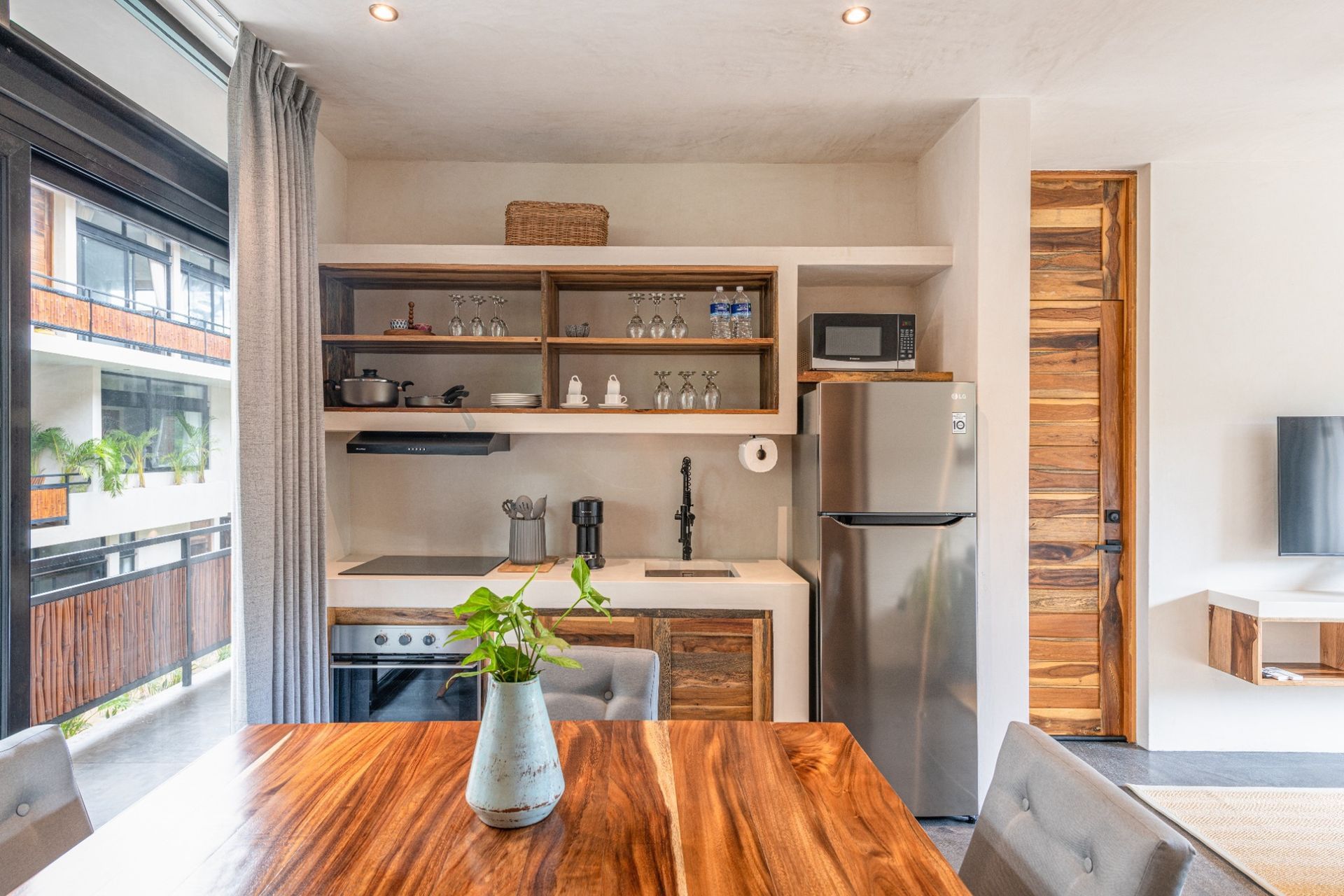 Bright modern kitchen with wooden table, open shelves, stainless fridge, and large window views