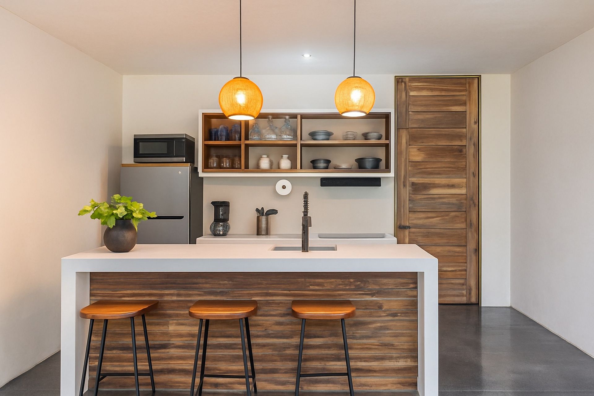 Modern kitchen with a white island, wooden stools, hanging lights, and open shelves.